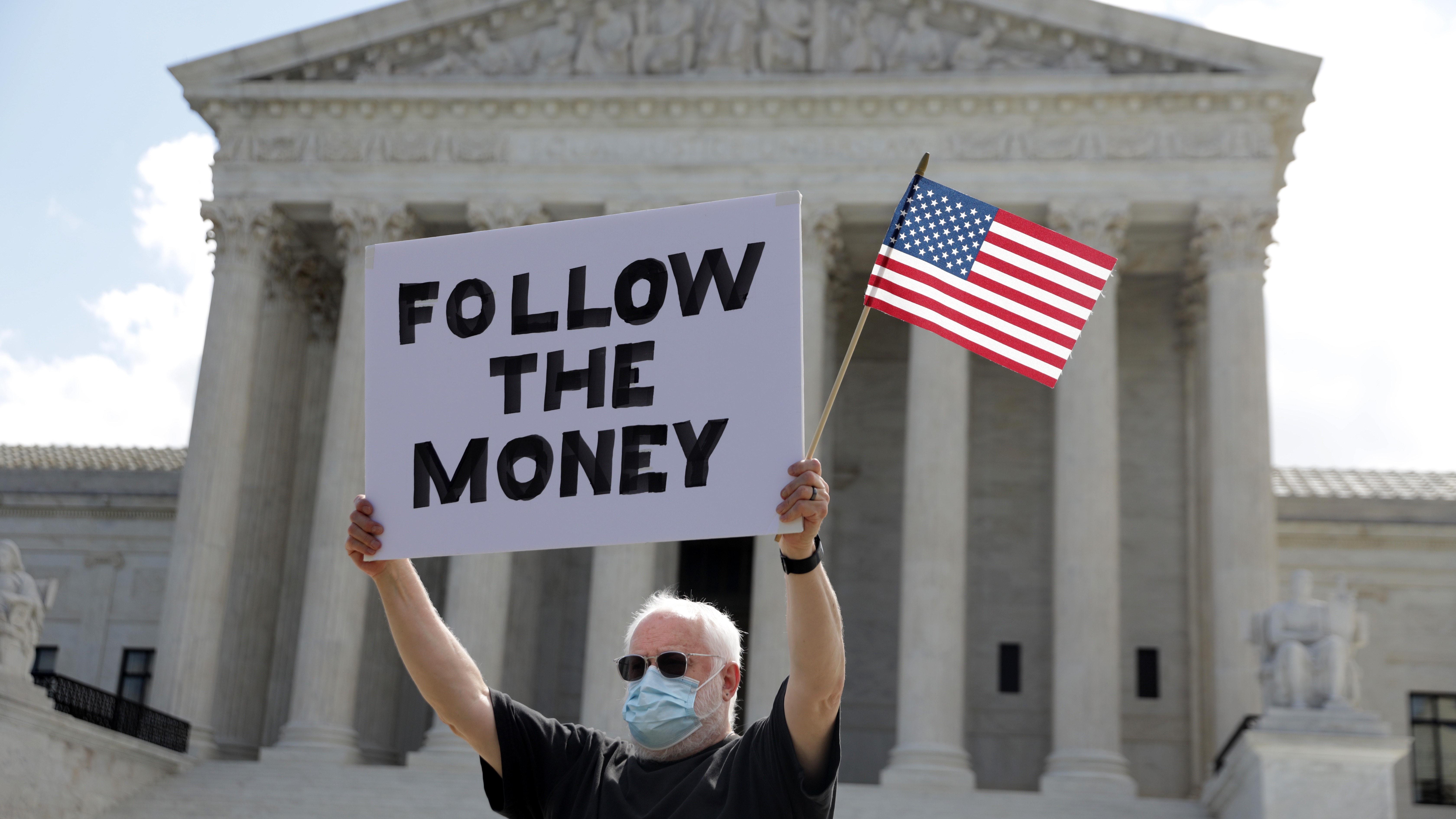 A man holds up a “Follow the Money” sign in front of the U.S. Supreme Court July 9, 2020.