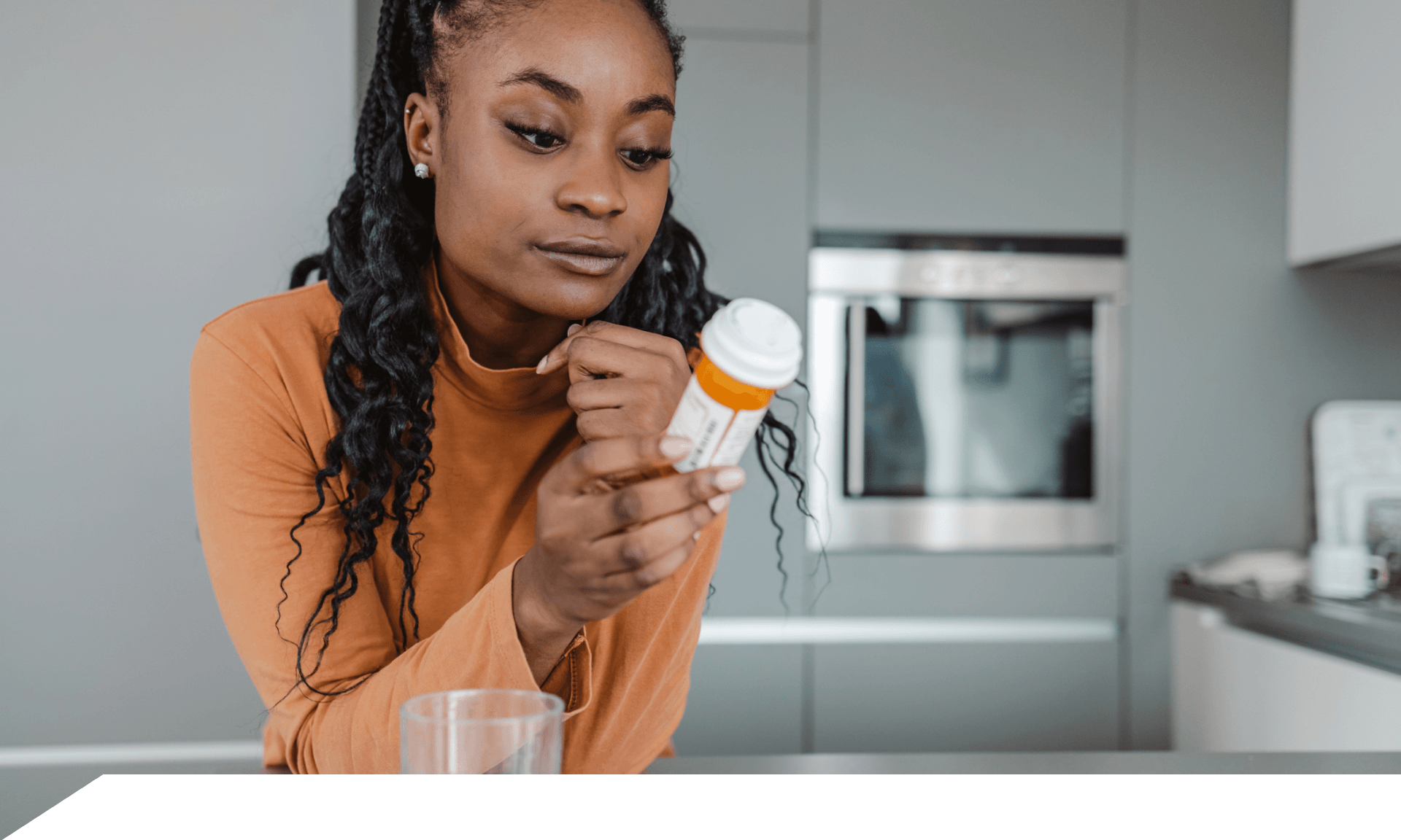 A woman leaning on a counter reading a bottle of pills