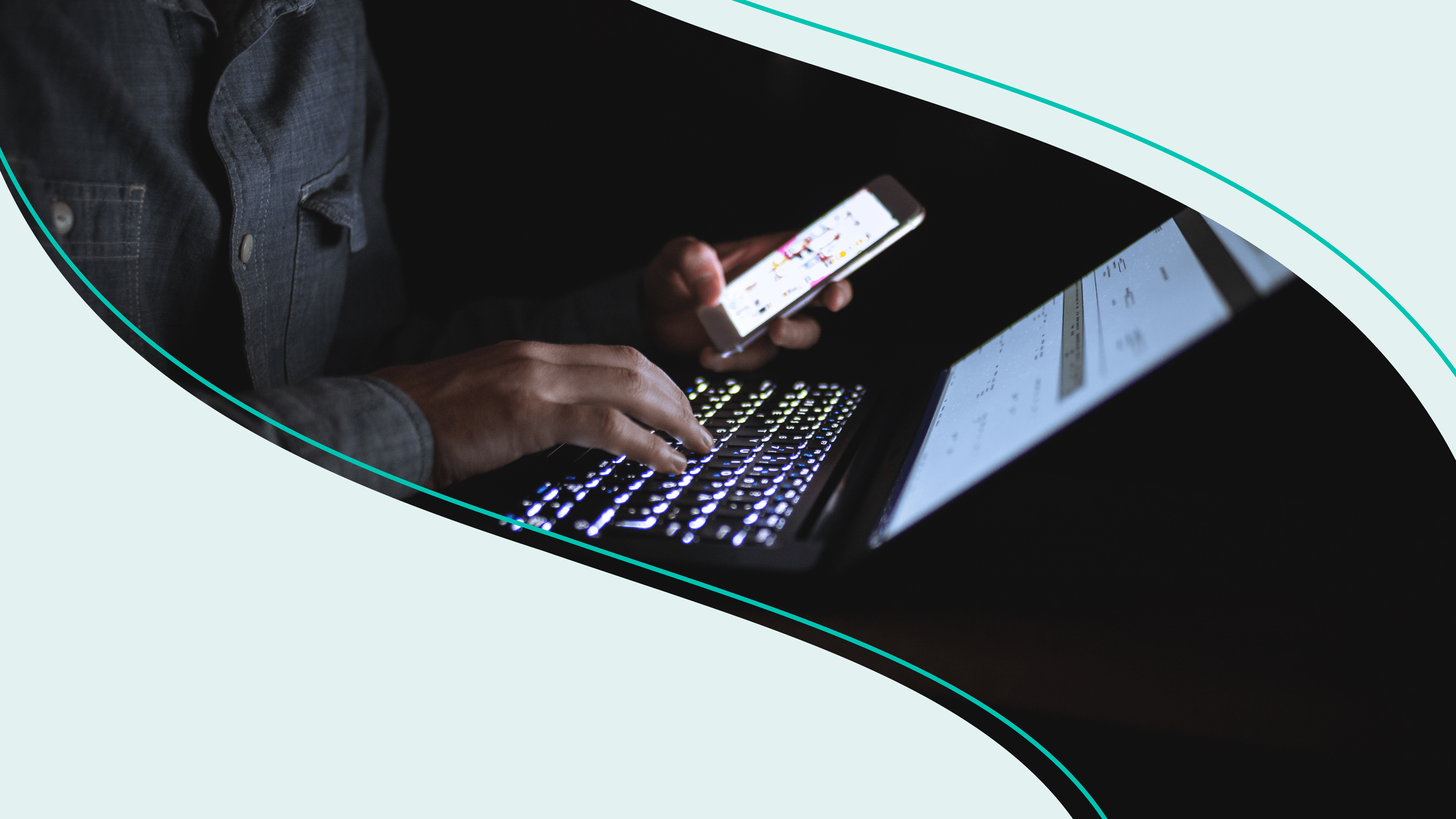 Someone holding a smartphone while typing on a computer