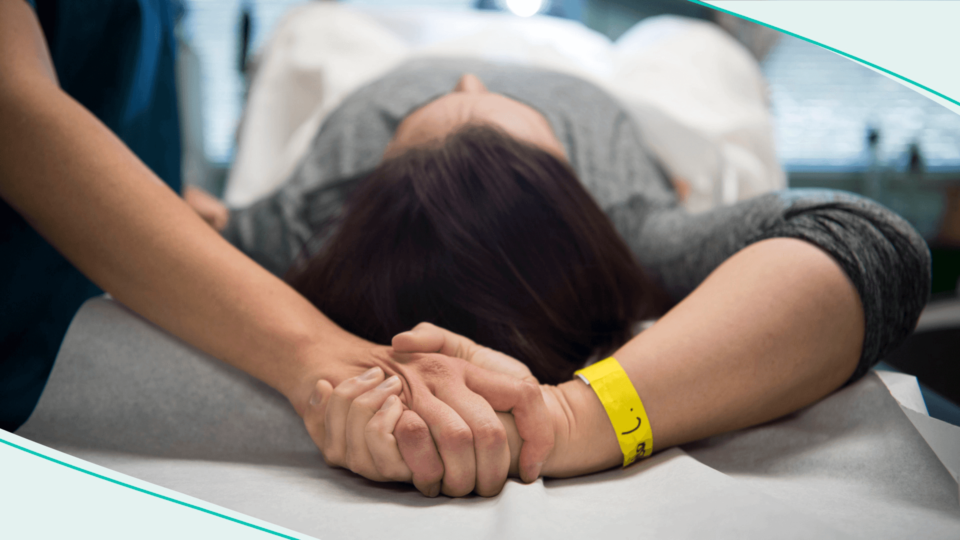 Two people hold hands while one is on a medical table
