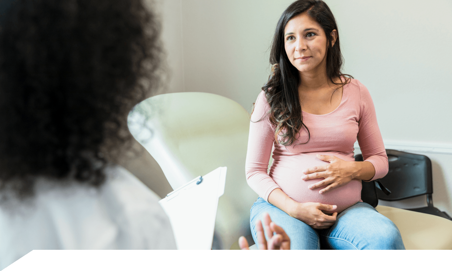 A woman with her hand over her pregnant belly facing her doctor