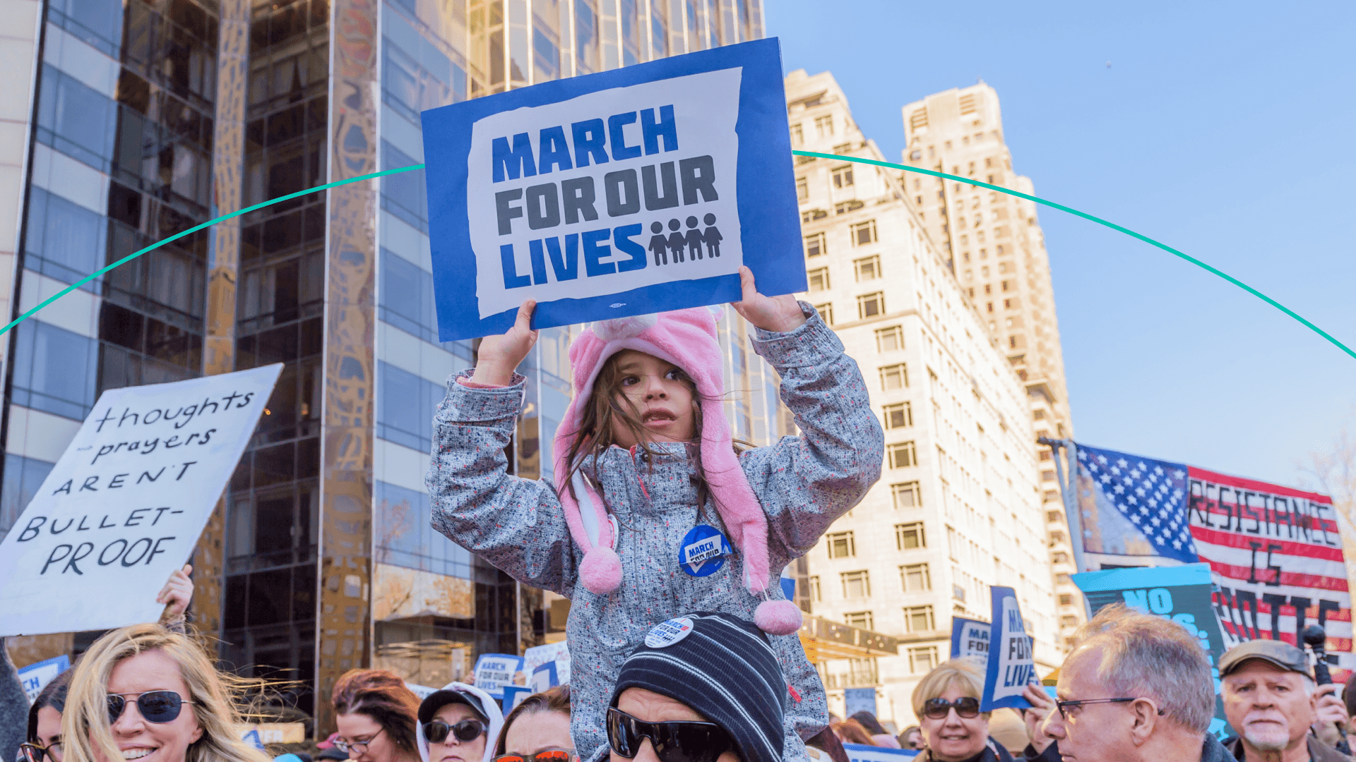 a young child holds up a march for our lives sign while being carried on a man's shoulders during an outdoor demonstration in New York