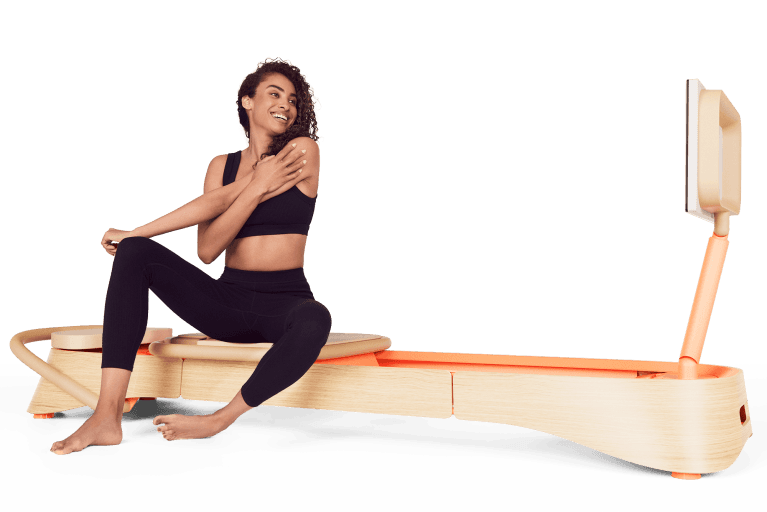 A person sitting on a pink frame reformer at-home pilates equipment