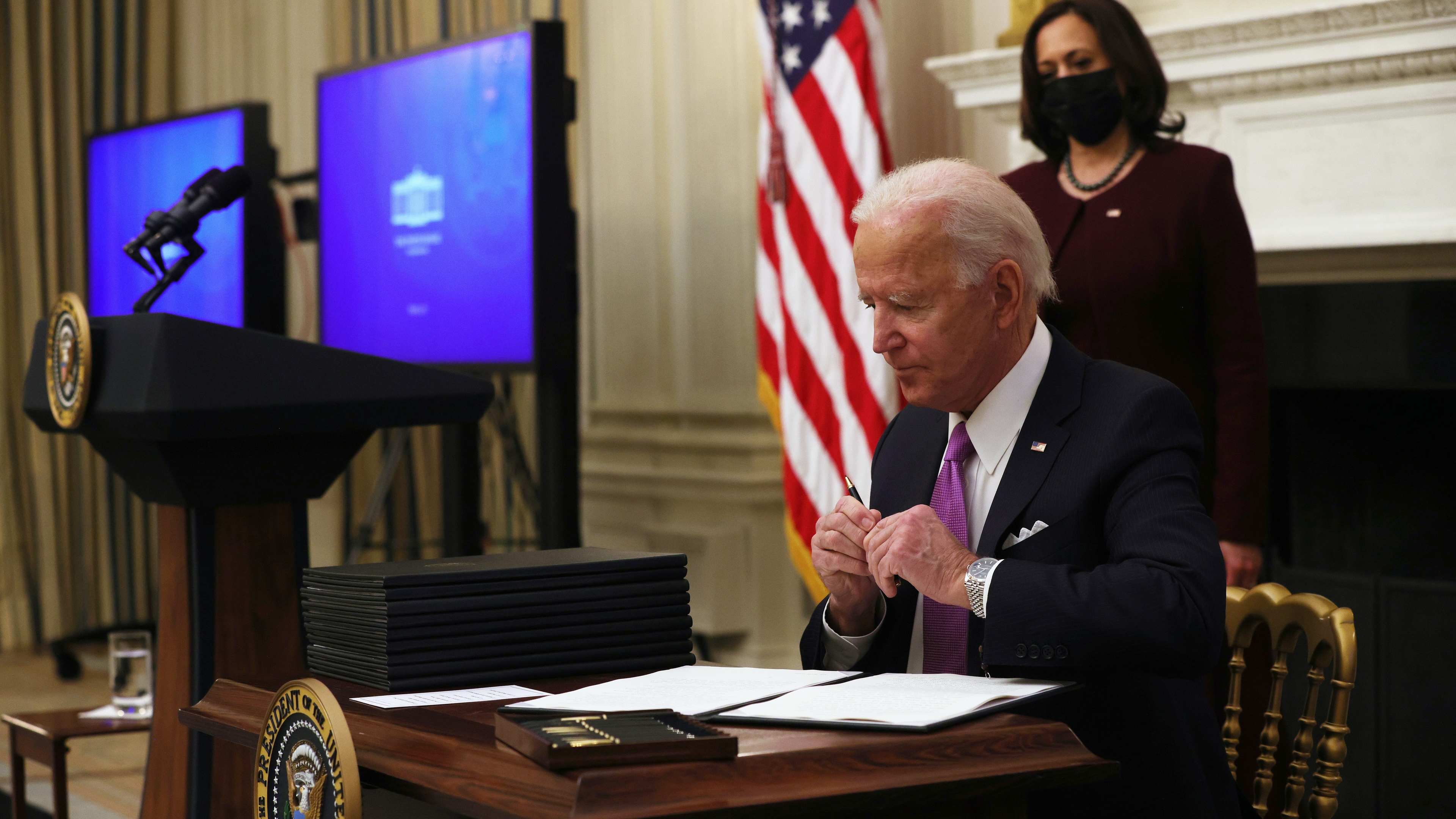 U.S. President Joe Biden signs executive orders as Vice President Kamala Harris looks on during an event at the State Dining Room of the White House January 21, 2021.